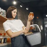 Kobieta w sklepie z koszykiem zastanawia się, czy ten miód to nie fałszowanie.