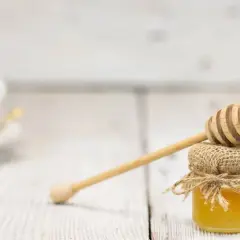Mały słoiczek miodu, naturalnego źródła węglowodanów, z drewnianą chochlą. W tle biała filiżanka.
