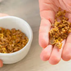 Garść naturalnego propolisu na dłoni, obok miseczki z tym pszczelim produktem. Propolis na skórę to cenny dar natury.