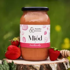 Słoik miodu truskawkowego z pasieki rodzinnej, otoczony świeżymi truskawkami i drewnianą chochlą.