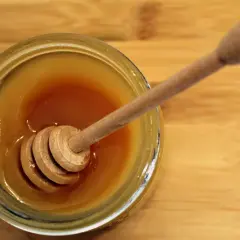 Słoik ze złotym miodem i drewnianą chochlą. Piana na miodzie tworzy delikatną warstwę.