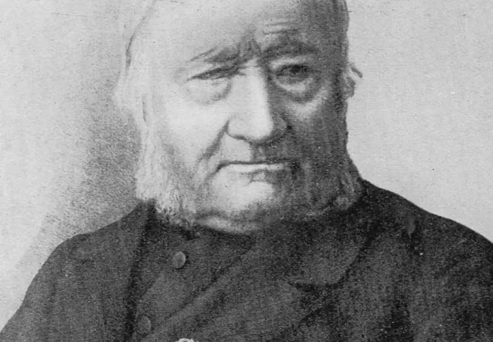 Portret Jana Dzierżona, pszczelarza z charakterystyczną brodą i siwymi włosami, w ciemnym stroju.