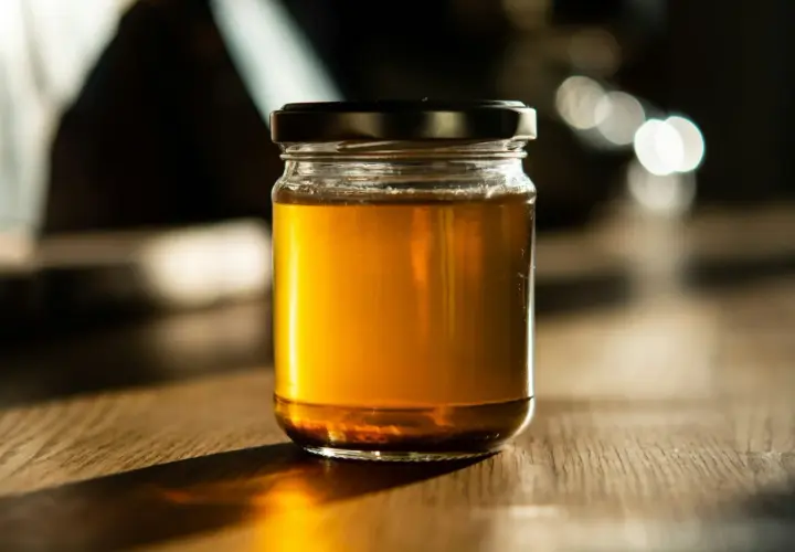 Słoik złocistego miodu na drewnianym stole. Czy miód nawilża gardło? Ten naturalny produkt może przynieść ulgę.