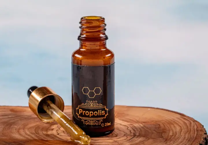 Propolis na zapalenie jelita grubego. Krople z propolisu w buteleczce z pipetą, na drewnianym tle.