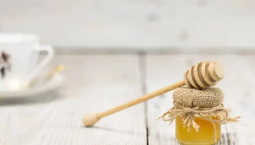 Mały słoiczek miodu, naturalnego źródła węglowodanów, z drewnianą chochlą. W tle biała filiżanka.