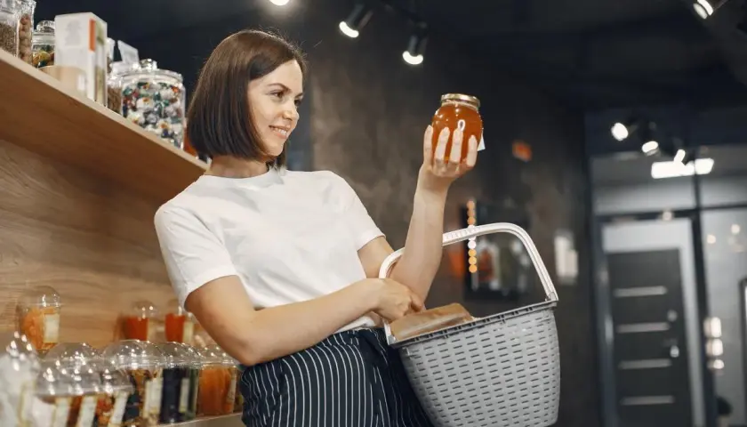 Kobieta w sklepie z koszykiem zastanawia się, czy ten miód to nie fałszowanie.