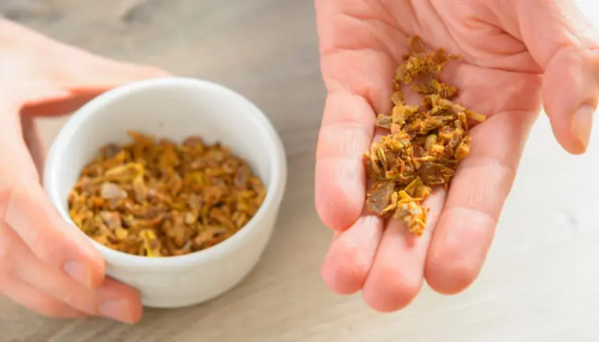 Garść naturalnego propolisu na dłoni, obok miseczki z tym pszczelim produktem. Propolis na skórę to cenny dar natury.