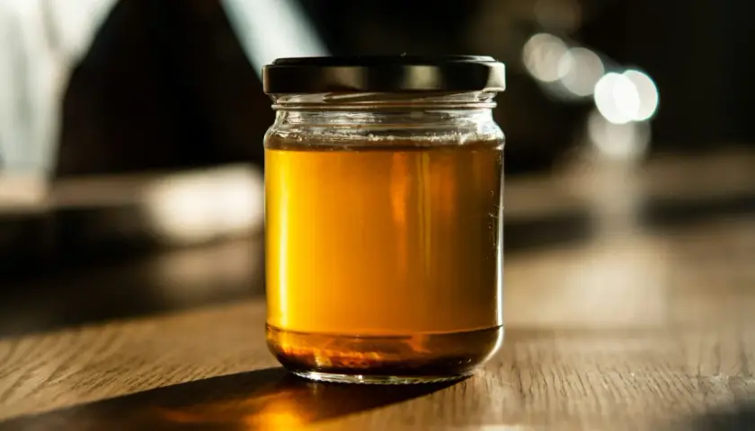 Słoik złocistego miodu na drewnianym stole. Czy miód nawilża gardło? Ten naturalny produkt może przynieść ulgę.