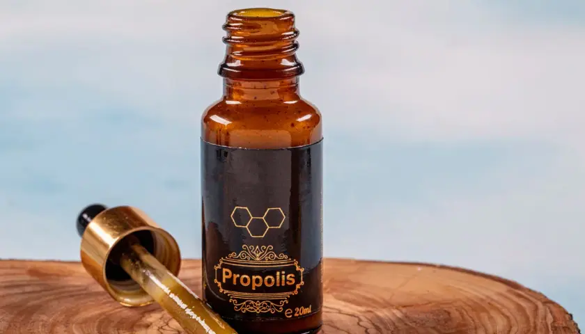 Propolis na zapalenie jelita grubego. Krople z propolisu w buteleczce z pipetą, na drewnianym tle.
