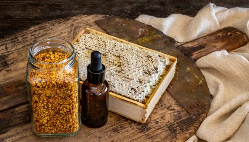 Słoik z pyłkiem pszczelim, buteleczka z kroplomierzem i plaster miodu. Naturalne składniki, które mogą posłużyć jako propolis lek.
