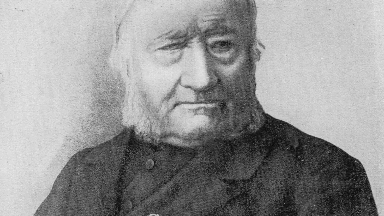 Portret Jana Dzierżona, pszczelarza z charakterystyczną brodą i siwymi włosami, w ciemnym stroju.